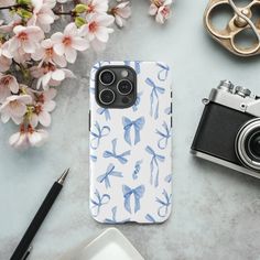 an iphone case sitting on top of a table next to a camera and some flowers