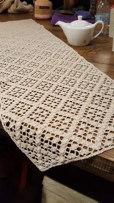 a crocheted table runner sitting on top of a wooden table next to a tea pot