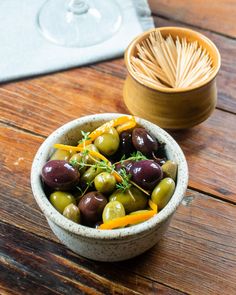 a bowl filled with olives and peppers on top of a wooden table