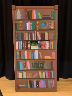 a book shelf filled with lots of books on top of a hard wood floor next to a black curtain