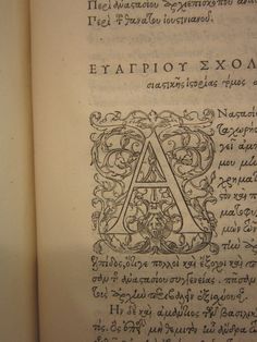 an open book with writing on it and the initial letter a in latin letters, surrounded by ornamental designs