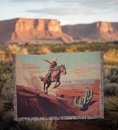 a blanket hanging from a clothes line with a cowboy on a horse in the desert