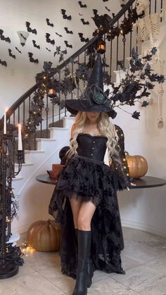 a woman dressed up as a witch sitting on a table in front of some stairs