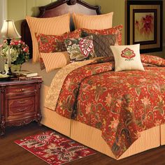 a bed with red and gold comforters in a bedroom next to a night stand