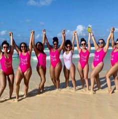 a group of women standing on top of a sandy beach next to the ocean with their arms in the air