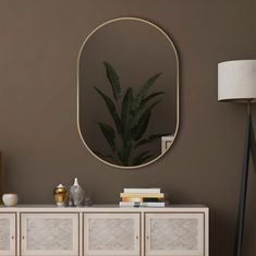 an oval mirror on the wall above a white sideboard with a plant in it