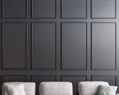 two white couches sitting next to each other in front of a black wall with vertical paneling