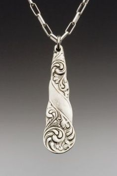 a silver pendant with an intricate design on it's side, hanging from a chain