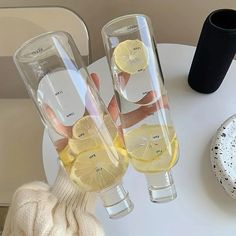 two wine glasses with lemon slices in them sitting on a table next to a vase