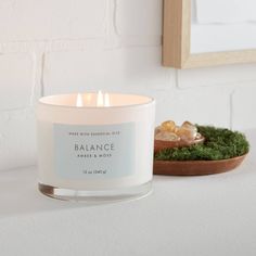 a white candle sitting on top of a table next to a bowl filled with moss