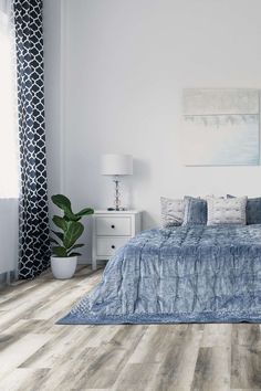 a bedroom with white walls and wood flooring is pictured in this image, there is a large bed that has blue sheets on it