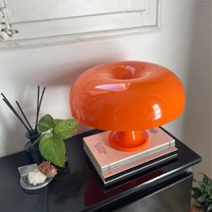 an orange lamp sitting on top of a black table next to a potted plant