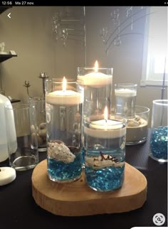 two candles sitting on top of a wooden plate filled with water and rocks in glass vases