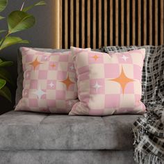 two pink and white pillows sitting on top of a couch next to a green plant