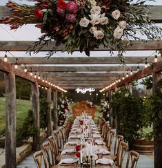 an outdoor dining table set up with flowers and greenery hanging from the pergolated roof