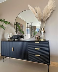 a black and gold sideboard with a mirror on the wall next to some plants