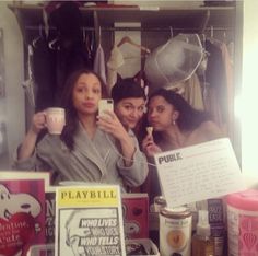 three women standing in front of a shelf holding cups and looking at their cell phones