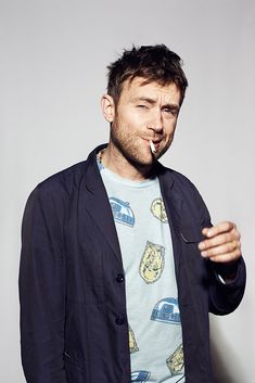 a man with a toothbrush in his mouth is posing for the camera while wearing a blue jacket