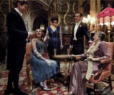 a group of people standing and sitting around a table in a room with chandeliers