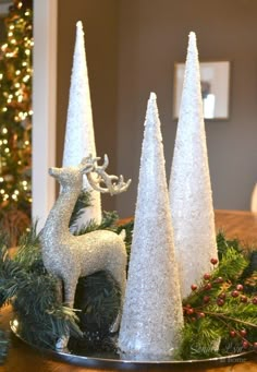 three white christmas trees sitting on top of a wooden table next to a silver deer