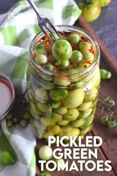 pickled green tomatoes in a glass jar with a spoon