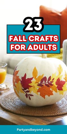 a white pumpkin sitting on top of a wooden table with fall leaves painted on it