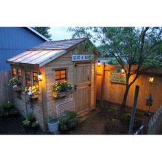 a small wooden building with lights on the windows and flowers growing in it's window boxes