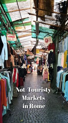 an outdoor market with lots of clothes and clothing hanging on the racks, in front of a sign that says not touristy markets in rome