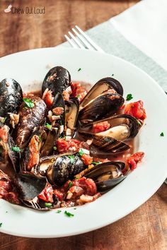 a white plate topped with mussels covered in sauce and parsley next to a fork