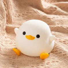 a small white plastic toy with black eyes and yellow feet sitting on a beige cloth