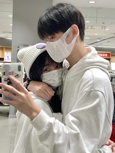 a man and woman wearing face masks while looking at their cell phones in an airport