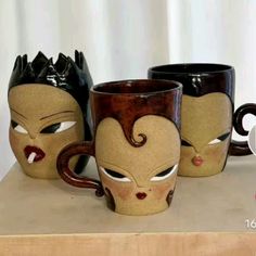 three coffee mugs with faces painted on them