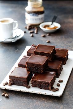 chocolate brownies on a white plate with coffee in the background