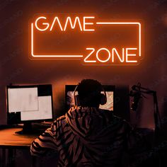 a man sitting at a desk in front of a neon sign that says game zone