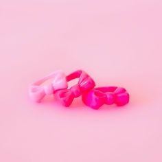 three pink and white bows are sitting on the ground, against a light pink background