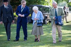 three older people standing in the grass looking at their cell phones while others look on