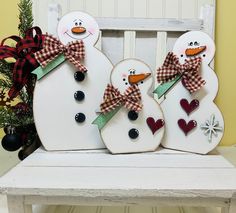 three snowmen sitting on top of a bench next to a christmas tree