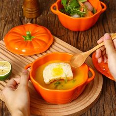 someone is eating soup from an orange bowl on a wooden tray with limes and tomatoes