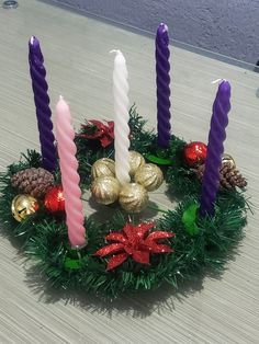 four candles are arranged in a wreath with ornaments around them on a table top, surrounded by pine cones and tinsel