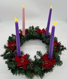 a wreath with three lit candles on top of it, surrounded by pine cones and poinsettis