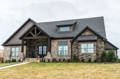 a house that is in the middle of some grass and has stone on it's front