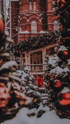 christmas trees are lined up in front of a building with red balls hanging from it