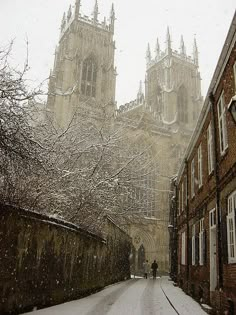 a snow covered street in front of a large building with two towers on each side