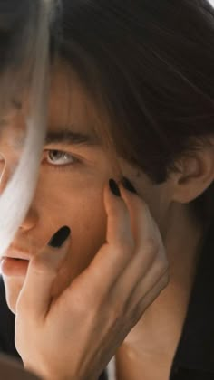 a woman with black nail polish holding her hand to her face and looking at the camera