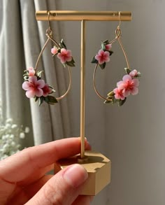 a hand holding a pair of earrings with pink flowers on the hoop and green leaves