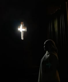 a person standing in the dark with a cross hanging from it's wall behind them