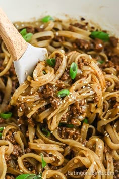 noodles with ground beef and green onions in a white bowl being stirred with a wooden spoon