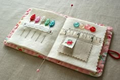 an open book with pins and buttons on it sitting on top of a tablecloth