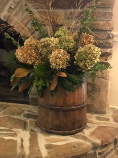 a wooden bucket filled with lots of flowers on top of a stone fireplace mantel