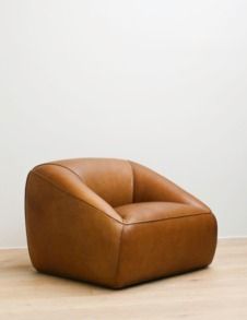 a brown leather chair sitting on top of a wooden floor next to a white wall